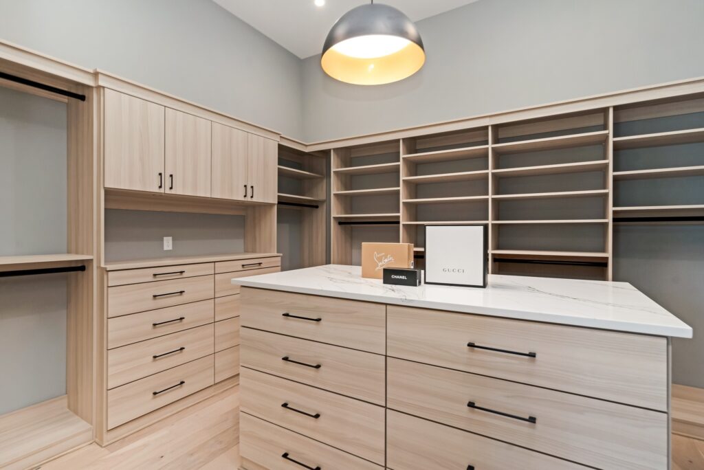 A Scandinavian-inspired closet with light wood cabinetry and a stylish center island under a modern dome light by Destination Cabinets.