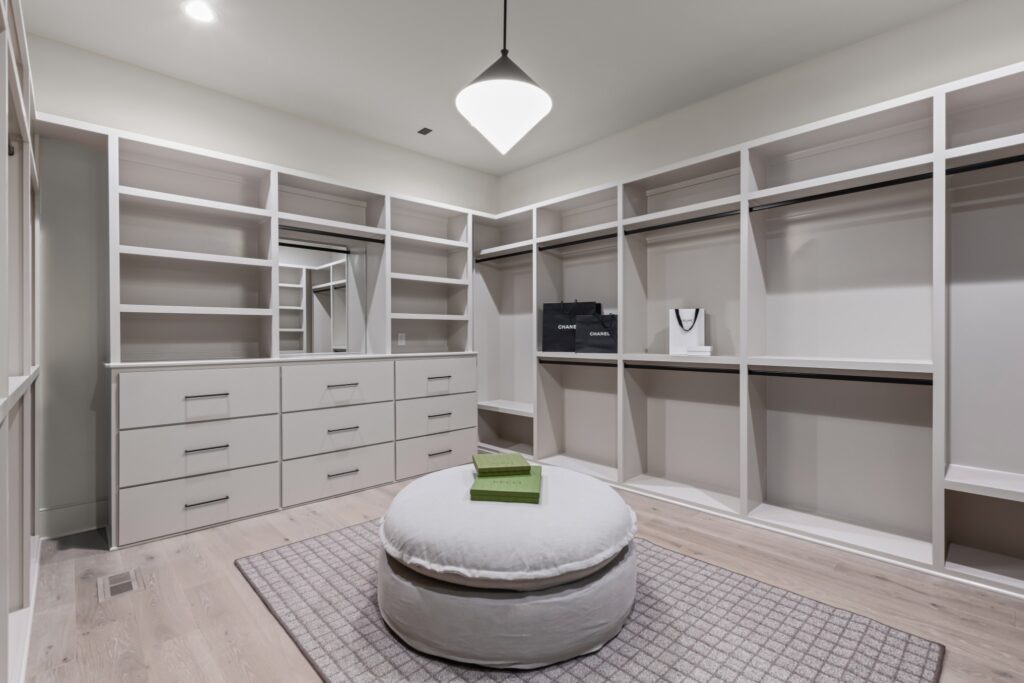 A spacious closet featuring white cabinetry, a plush ottoman, and designer accessories by Destination Cabinets.