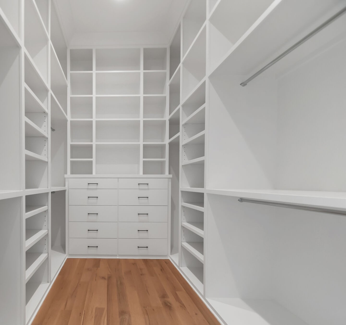 A minimalist white closet featuring extensive shelving, drawers, and hanging space by Destination Cabinets.