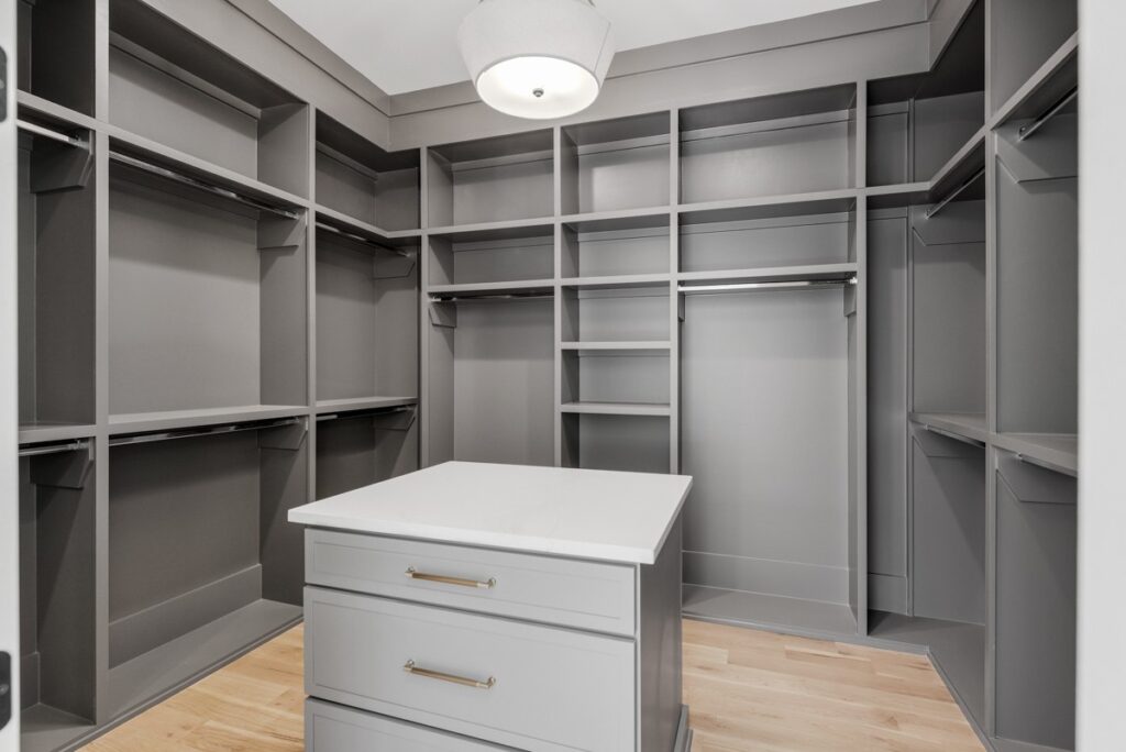 A well-crafted closet featuring a central island with drawers and surrounding gray shelving units by Destination Cabinets.