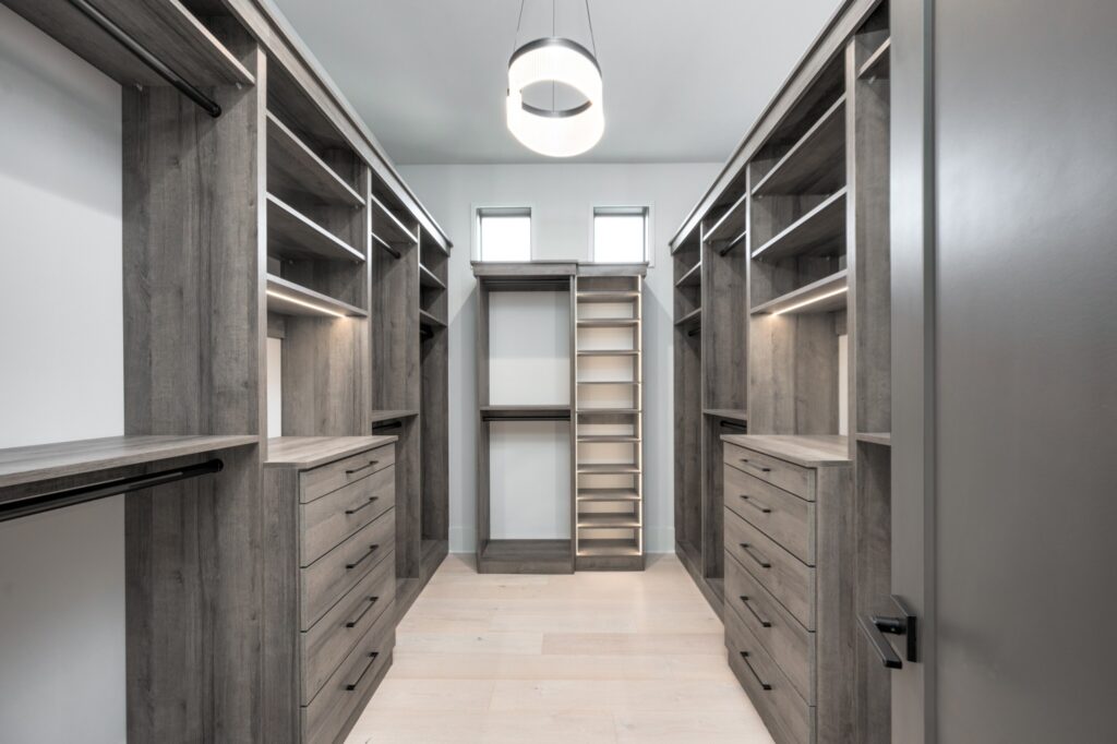 A modern closet showcasing gray wood finish cabinetry with sleek hardware and ambient lighting by Destination Cabinets.