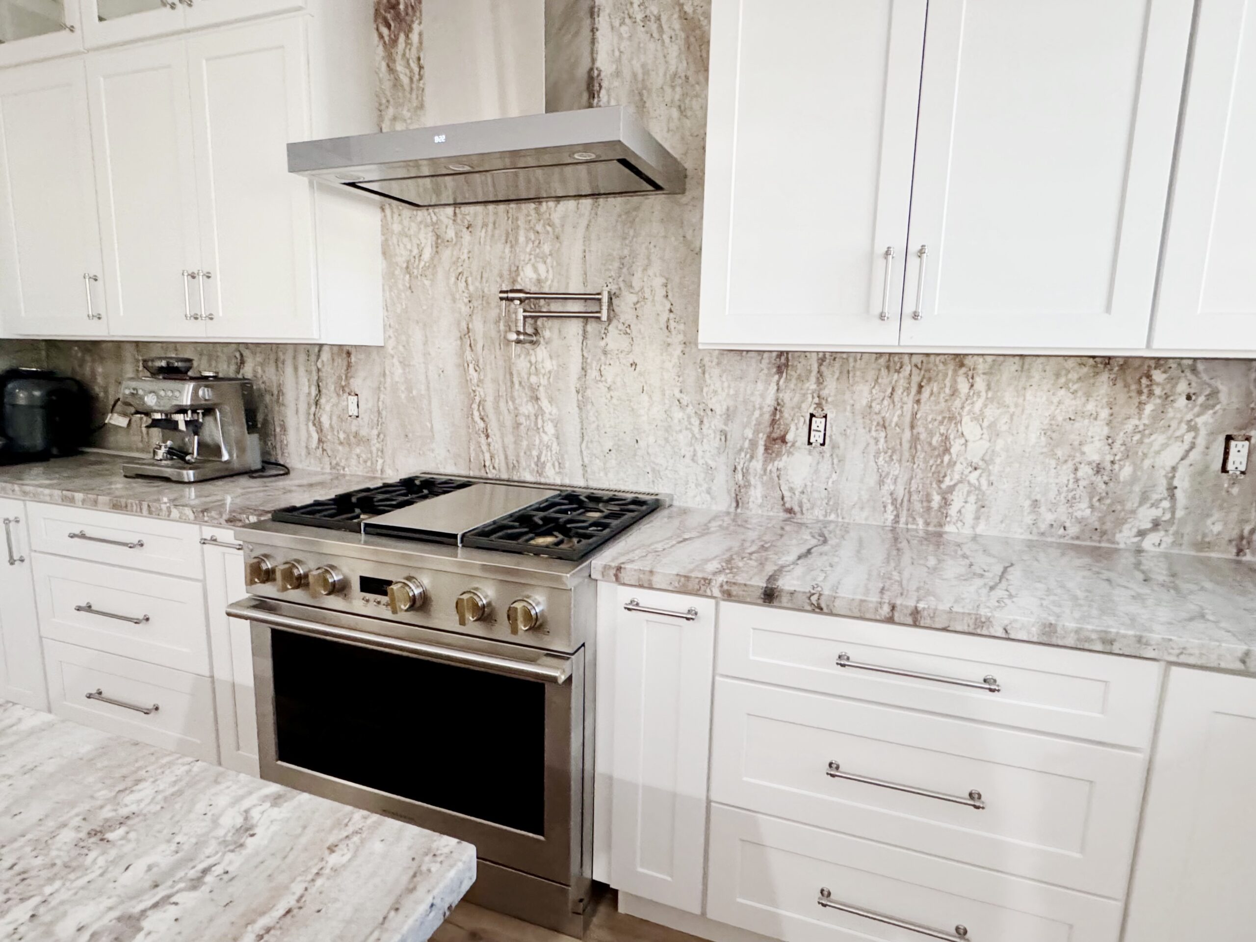 Luxurious kitchen with white cabinetry, marble backsplash, and professional-grade stove and hood.