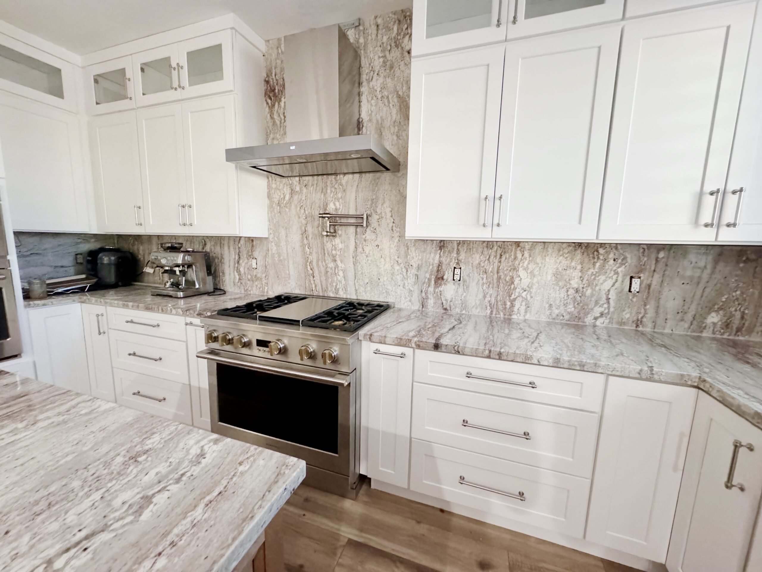 Upgraded kitchen with white cabinets, stainless steel stove and range hood, and marble backsplash.