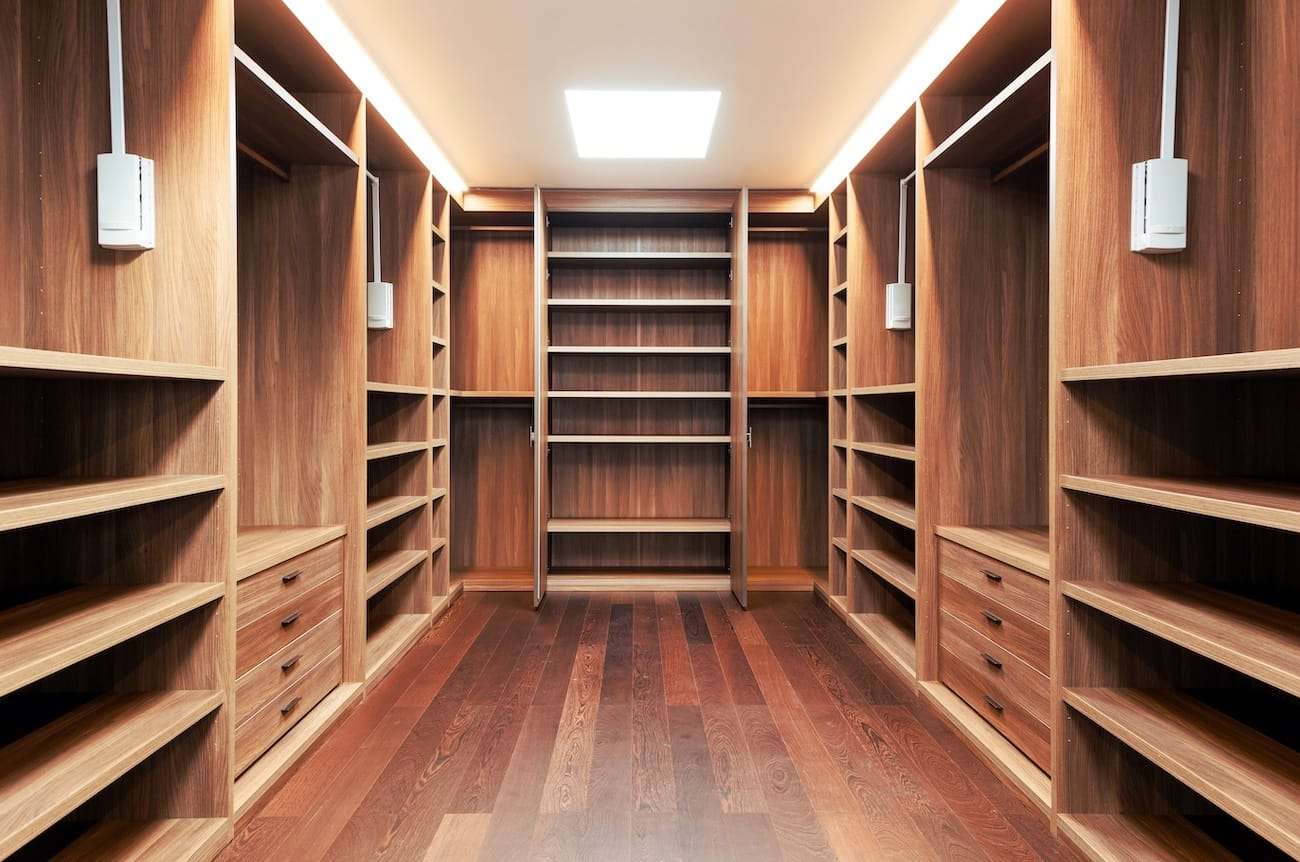 An inviting walk-in closet with walnut shelving, integrated lighting, and built-in drawers by Destination Cabinets.