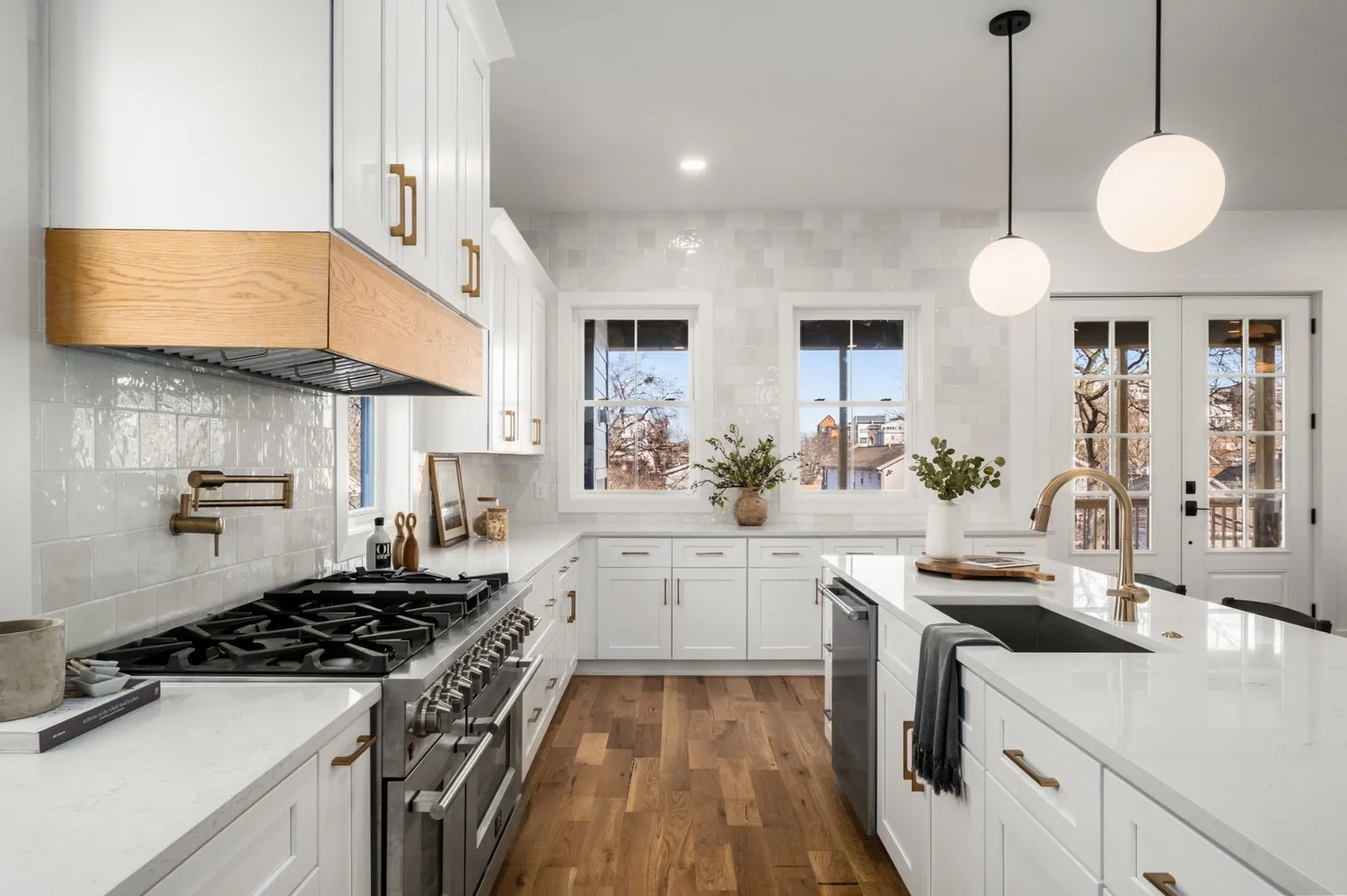 Chic white kitchen with oak wood accents, marble countertops, and globe pendant lights with a view outdoors.