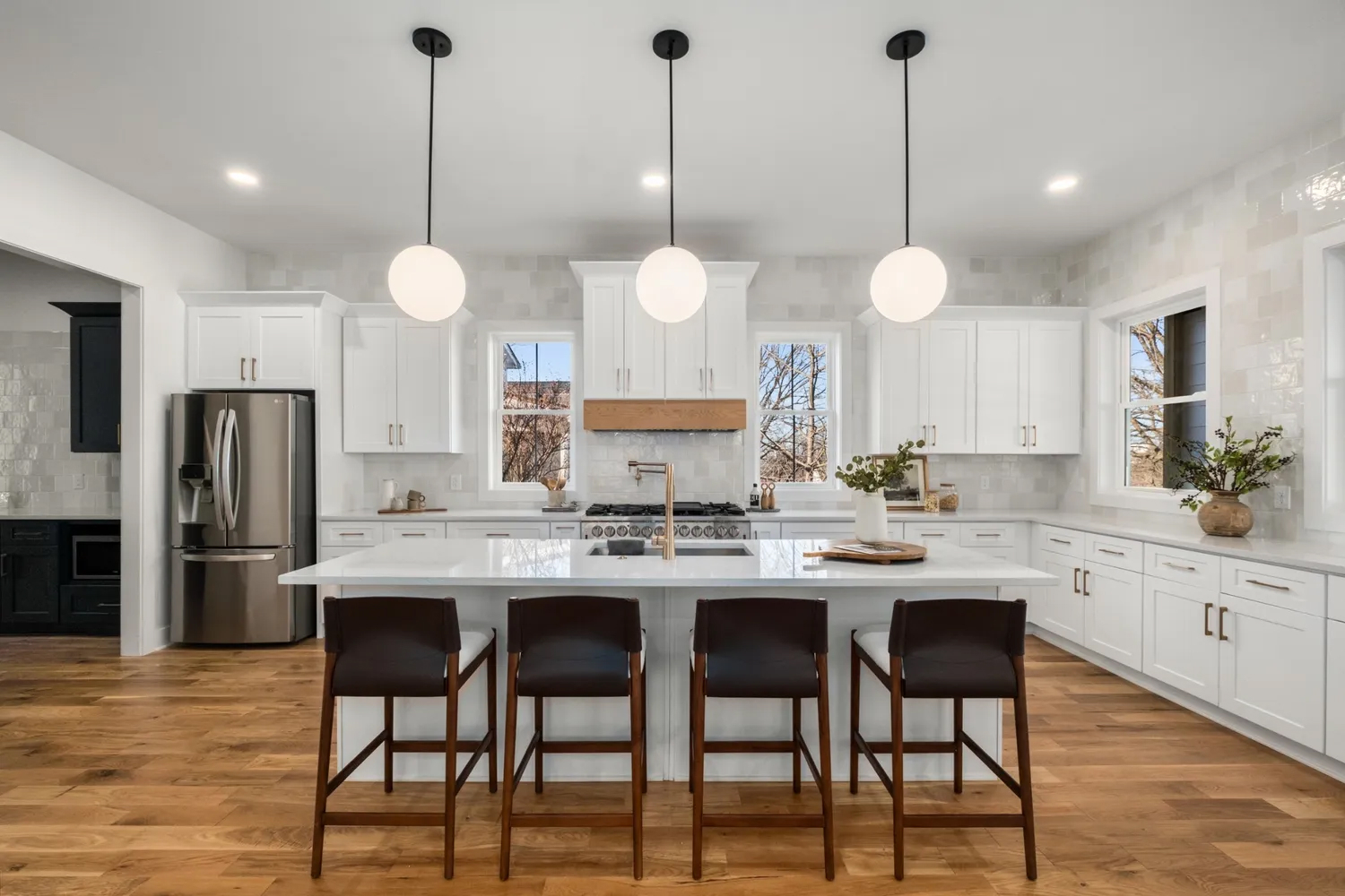 Modern white kitchen with hardwood floors, marble island, and three globe pendant lights.