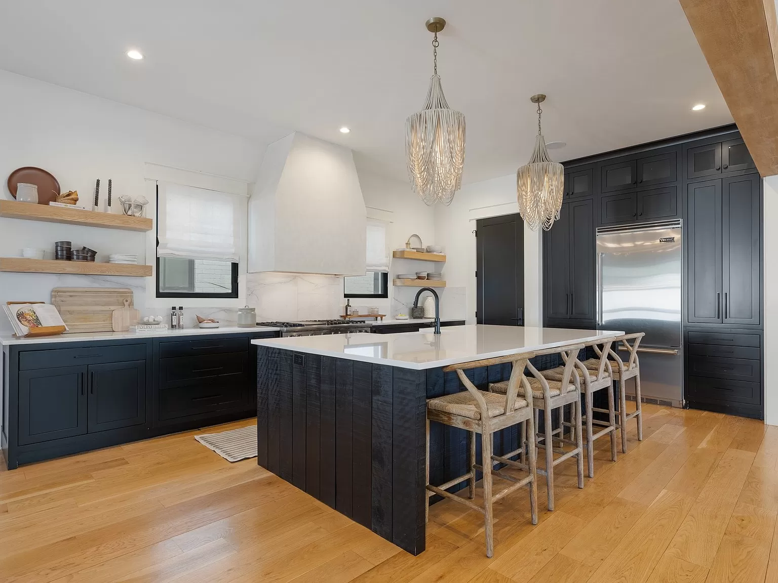 Open kitchen with a large island, navy cabinets, and hanging teardrop chandeliers.