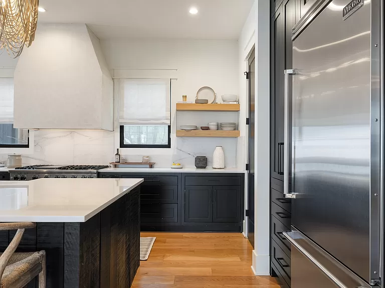 Sleek kitchen corner with navy cabinetry, marble countertops, and chic open shelving.