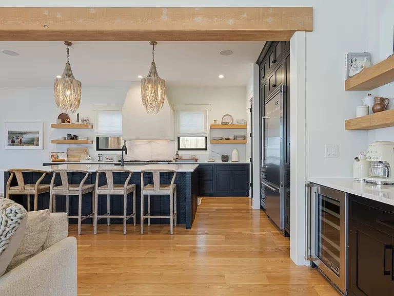 Open kitchen space with a wood beam, two elegant chandeliers, and navy blue island cabinetry.