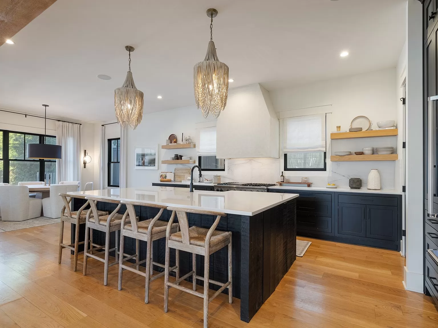 Spacious kitchen with elegant teardrop chandeliers, a black island, and woven bar stools.