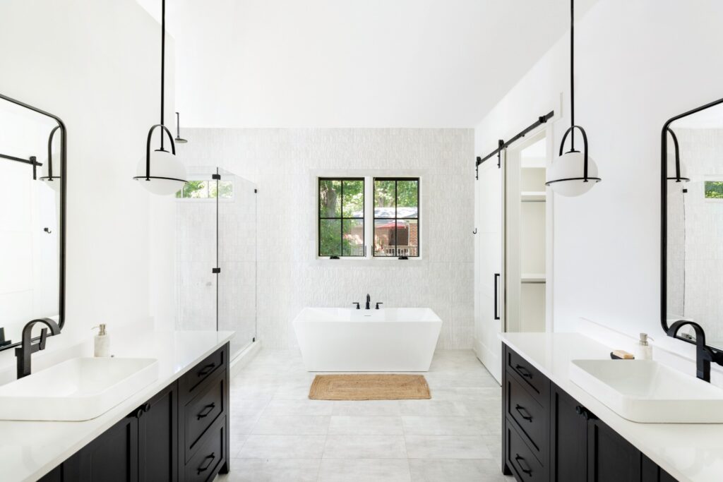 A contemporary monochrome bathroom with sleek black vanities, white countertops, and statement pendant lights by Destination Cabinets.