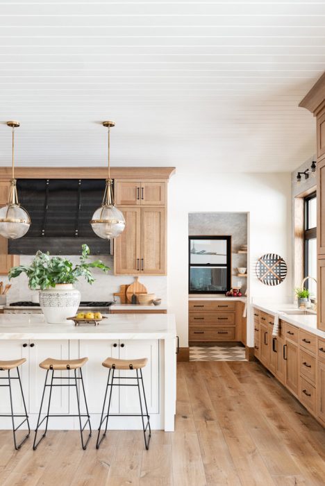 Warm wooden cabinetry with black accents in a bright kitchen, featuring hanging globe lights.